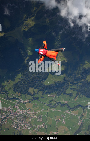 Skydiver within a special wingsuit is flying along a cloud edge over nice land scape scenery. The Birdman is going fast forward. Stock Photo