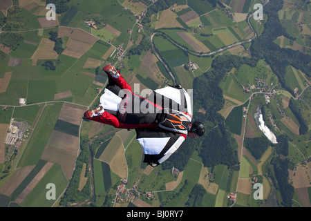 Skydiver within a special wingsuit is flying over a nice land scape scenery. The Birdman is going fast forward in the blue sky. Stock Photo