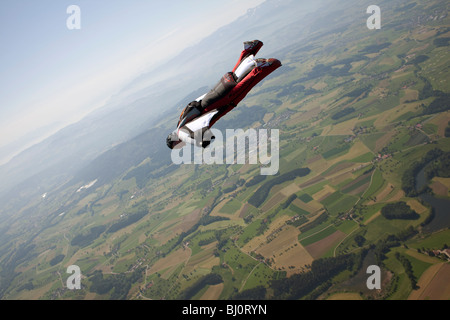 Skydiver within a special wingsuit is flying over a nice land scape scenery. The Birdman is going fast forward in the blue sky. Stock Photo