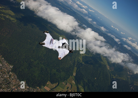 Skydiver within a special wingsuit is flying along a cloud edge over nice land scape scenery. The Birdman is going fast forward. Stock Photo