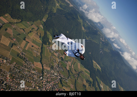 Skydiver within a special wingsuit is flying along a cloud edge over nice land scape scenery. The Birdman is going fast forward. Stock Photo