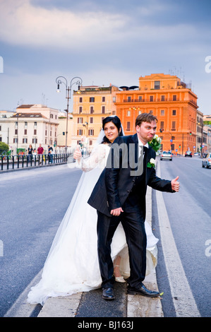 Bride and groom hitchhiking on road Stock Photo