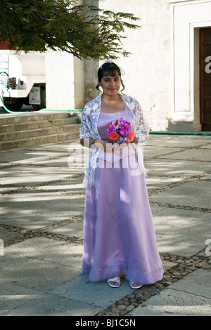 pretty Mexican teen standing in plaza outside Santo Domingo Church wearing  gown for her Quinceanera ceremony & holding flowers Stock Photo