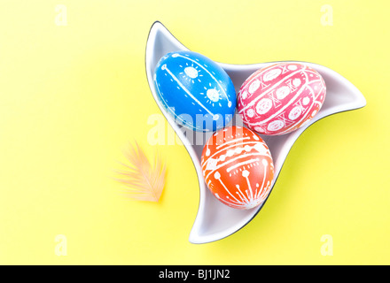 Colorful handmade Easter eggs in saucer with color feather isolated on yellow background Stock Photo
