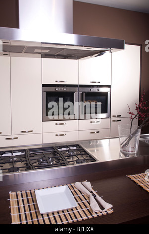 Modern kitchen with white polished cabinets and dark wooden counter beside the steel stove desk in the middle Stock Photo