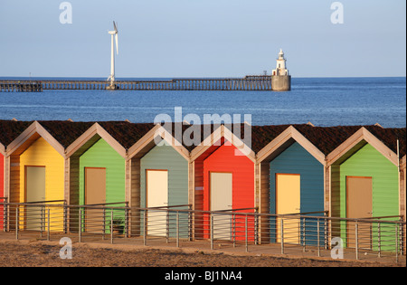 Beach huts at Blyth in Northumberland, England with the pier and a wind turbine in the background. Stock Photo