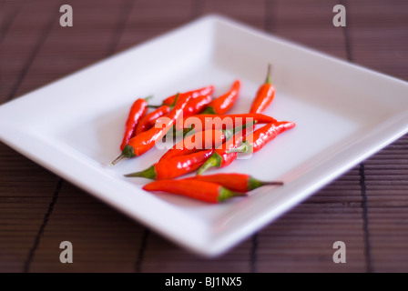 A square white plate of whole red chillis on a bamboo surface Stock Photo
