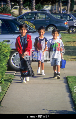 Hispanic boy in red jacket walks with twin brother and sister on way to school protect care love sibling Stock Photo