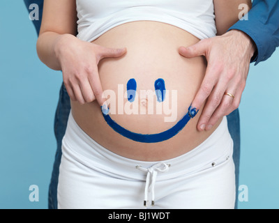 License available at MaximImages.com - Pregnant young woman and her husband painting a happy smiley face on her belly. Stock Photo