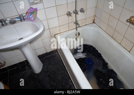 dirty washing in dirty water in a bath being washed in a run down bathroom Stock Photo