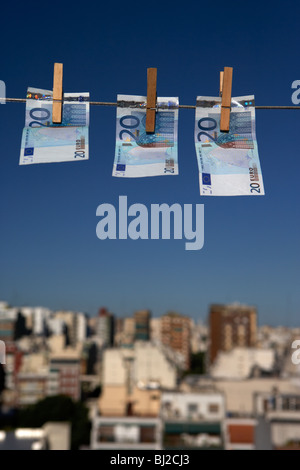 three twenty euro banknotes hanging on a washing line with blue sky over city skyline Stock Photo