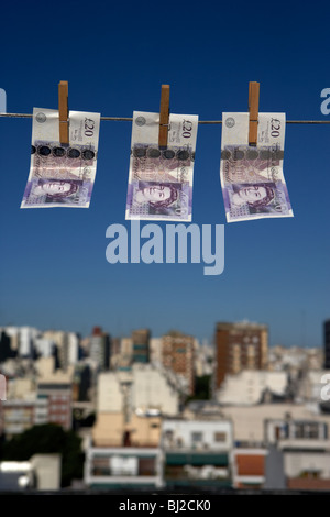 three twenty pounds sterling banknotes hanging on a washing line with blue sky above a city skyline