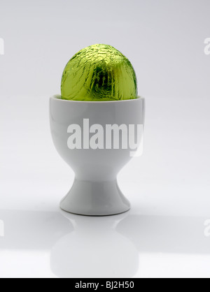 Brightly Green foil covered chocolate Easter egg in a white egg cup Stock Photo