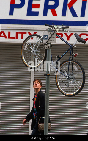 A bemused passer-by walks past a mountain bike positioned up on a parking pole in central London. Stock Photo