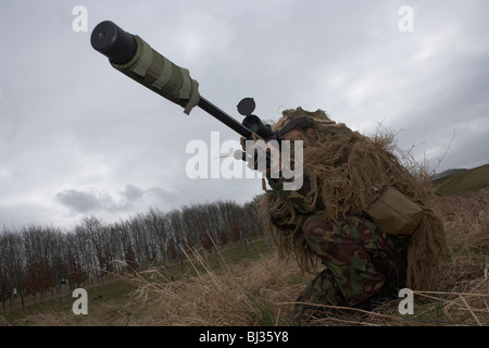 A camouflaged British infantry soldier is seen looking down the telescopic sight of a L115A3 sniper rifle. Stock Photo