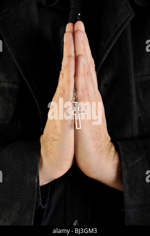 Praying hands holding a necklace with a cross pendant Stock Photo