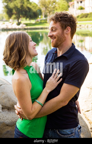 Attractive fun loving joyfully joyful Young couple in there 30s standing together looking at each other lakeside park content contentment contented Stock Photo