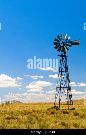 Windmill Rural New South Wales Australia | RURAL NEW SOUTH WALES, Australia — A steel lattice windpump with a visible tail vane stands in a dry paddock beside a wire fence. The vane automatically aligns the rotor into the wind, driving a mechanical piston pump that draws bore water to the surface for livestock in regions where rivers routinely run dry across Australia's pastoral interior. Stock Photo