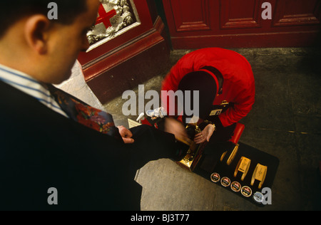 A businessman stands over a Victorian-style shoe-shiner in a corner of Leadenhall Market in the City of London. Stock Photo