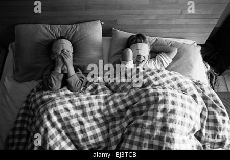 Looking down on them from above, we see a brother and sister play with free airline blindfolds while in their parents' bed. Stock Photo