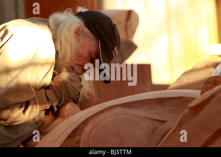 A man carving out a giant totem from a log in a workshop on Granville island in Vancouver British Columbia. Stock Photo