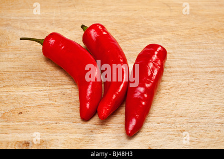three red chilli peppers on a chopping board Stock Photo