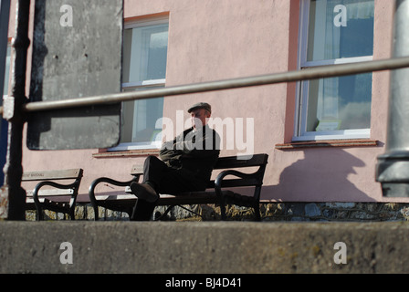 Old man on bench in front of pink house. Marine Parade, Lyme Regis, Dorset, England Stock Photo