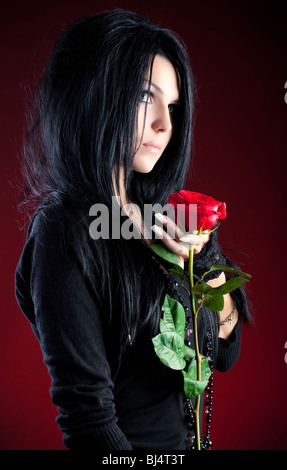 Young goth woman with red rose. On red background. Stock Photo