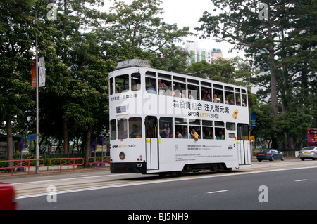 A Hong Tram in an all over advertising livery passes Victoria Park on Hong Kong Island Stock Photo