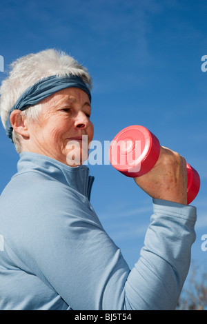Britain, UK, Europe. Grey haired senior woman exercising with dumbbell hand weights outdoors to prevent Alzheimer's disease. Stock Photo