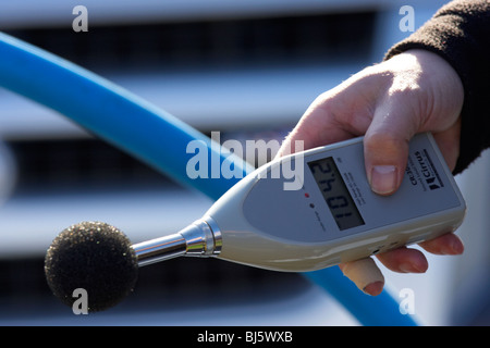 mans hand holding sound level meter with baffle showing measurement of 104.2 dB the meter is used to measure maximum noise Stock Photo