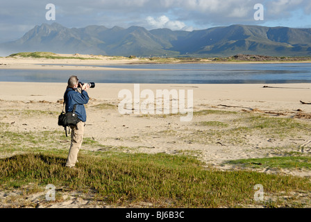 Man taking photograph of a landscape with telephoto in the morning, Flamingo lake estuary near Hermanus, South Africa Stock Photo