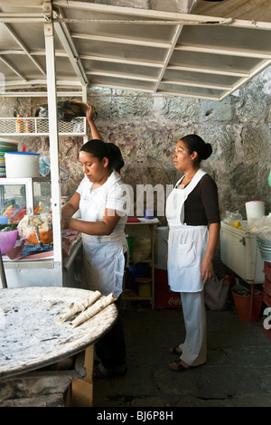 two young women with classic Indian faces preparing tacos to order at demountable sidewalk stand in Oaxaca City Mexico Stock Photo