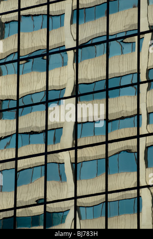 A concrete building reflected in the panes of glass on another office building. Stock Photo