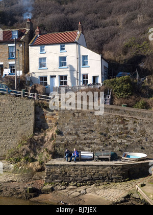 A couple sit in the spring sunshine at Cowbar, Staithes on the North Sea Coastal path and Cleveland Way long distance walk Stock Photo