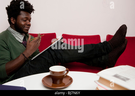 Man relaxing with cup of coffee, pen and notepad in a red sofa Stock Photo