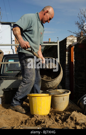 a self employed builder mixing cement , filling buckets, on the back of his truck, UK Stock Photo