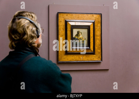 Male tourist wearing headphones / headphone guide looking at The Lacemaker painting by Vermeer. The Louvre Museum, Paris. France Stock Photo