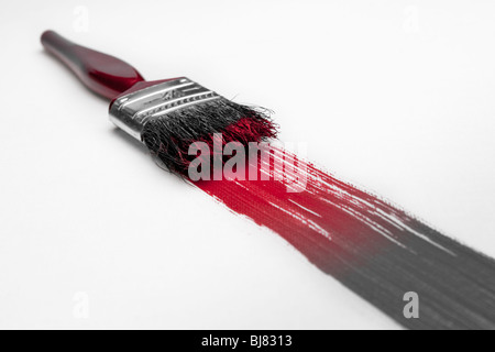 A paintbrush paints a line of paint that fades from grey to red. Stock Photo