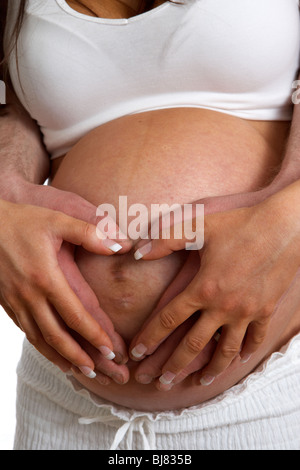8 month pregnant 30 year old woman with 37 year old male partner holding hands over baby bump Stock Photo