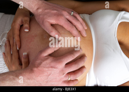 8 month pregnant 30 year old woman with 37 year old male partner hands on the bump Stock Photo