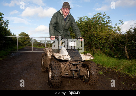 Senior farmer riding four wheeler behind a cow in a muddy field Stock ...