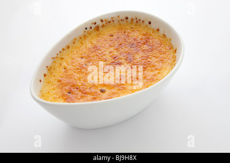 Golden-brown caramelized crème brûlée served in a white oval dish, isolated on a white background. Stock Photo
