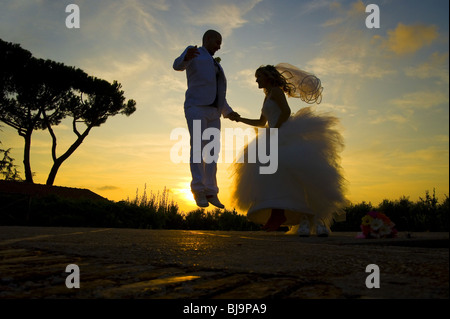 Bride and groom jumping for joy at sunset Stock Photo