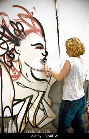 Rear view of young caucasian adult female graffiti artist with can of aerosol paint in hand, creating a piece of street art. Stock Photo