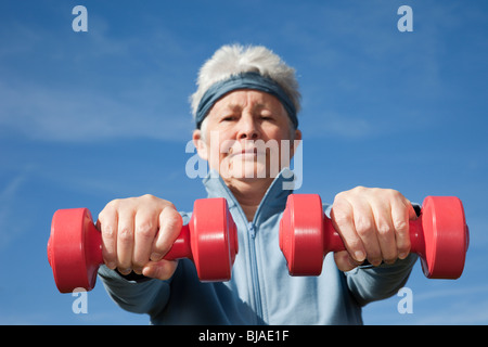Senior woman being active adult exercising with dumbbell hand weights workout outdoors to keep fit. Healthy lifestyle wellness concept. England UK Stock Photo