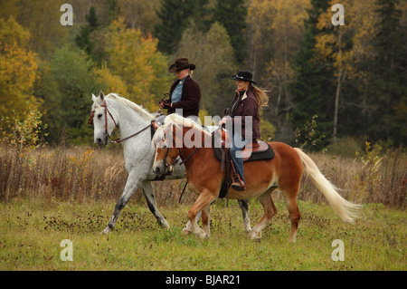 Two women dressed in cowboy clothes and hats riding horses western style on horseback at a ranch Stock Photo