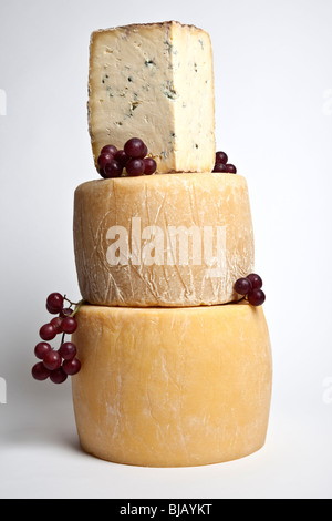 Two whole round cheeses with a large wedge of blue cheese in a tower with grapes Stock Photo