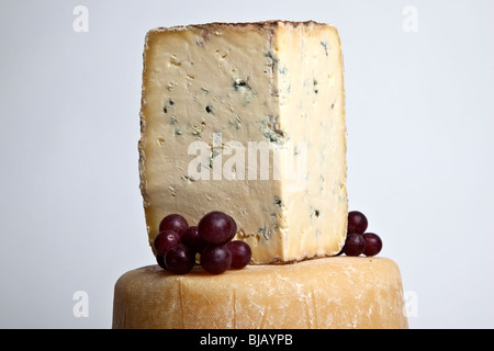 A whole round cheese with a large wedge of blue cheese in a tower with grapes Stock Photo