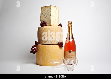 A celebration tower of whole round cheeses with a large wedge of blue cheese with a bottle of pink champagne and two glasses Stock Photo